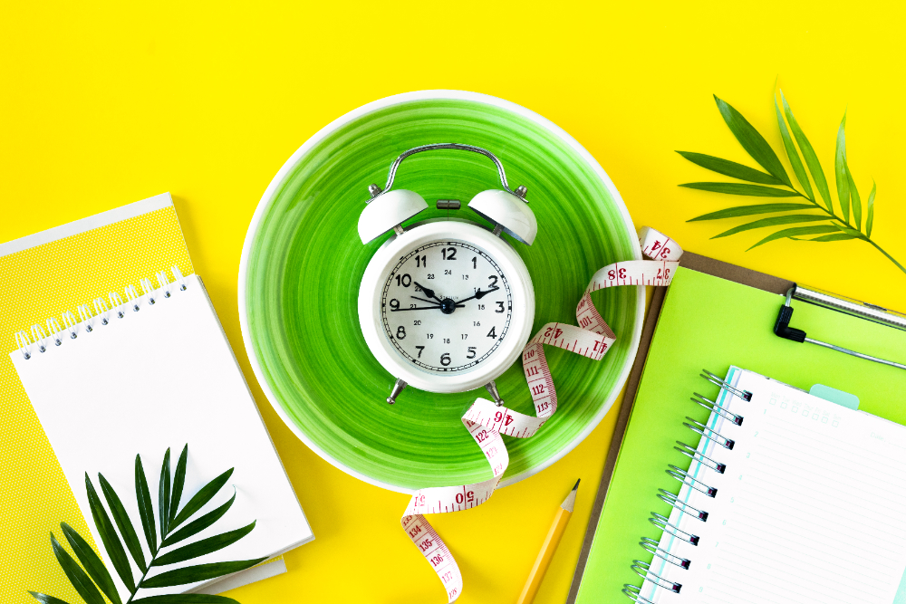Alarm clock in a plate with measuring tape as a symbol for intermittent fasting.