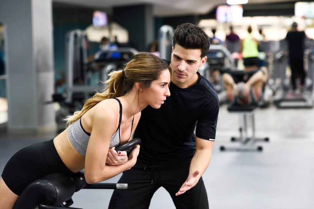 Girl working out with a personal trainer supporting her.