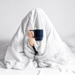 Woman with coffee and lack of motivation wrapped in blanket.